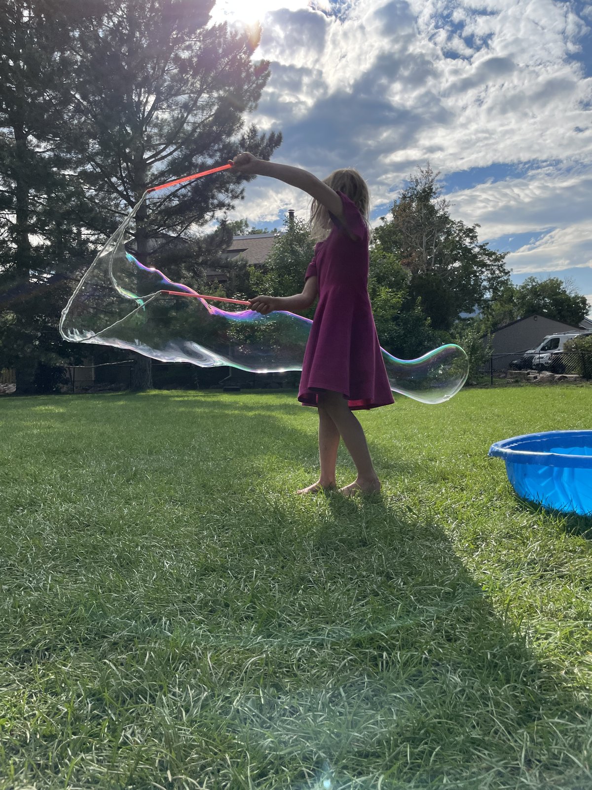 A child making a giant bubble in a sun-lit grassy yard