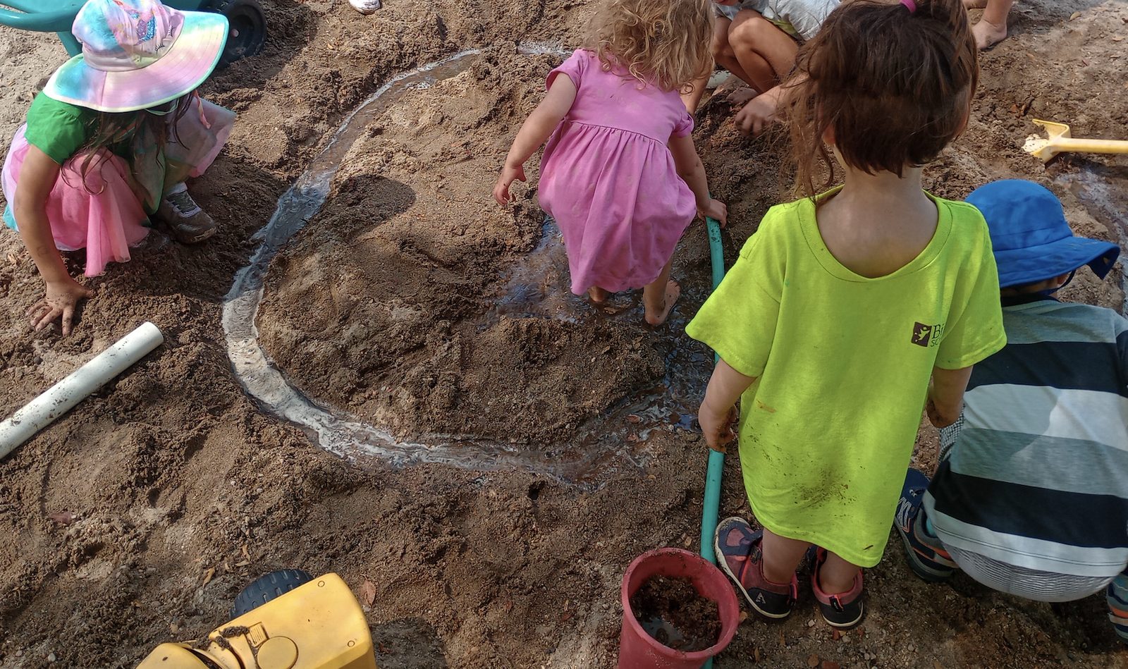 Children digging and channeling water through sand in an outdoor play area